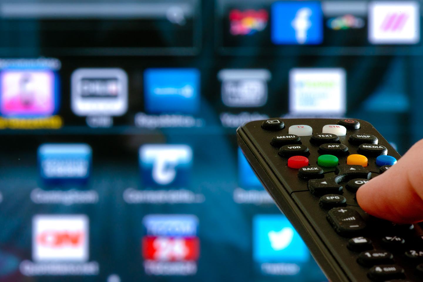 Fernbedienung mit HbbTV Knopf und im Hintergrund Smart-TV mit App-Icons